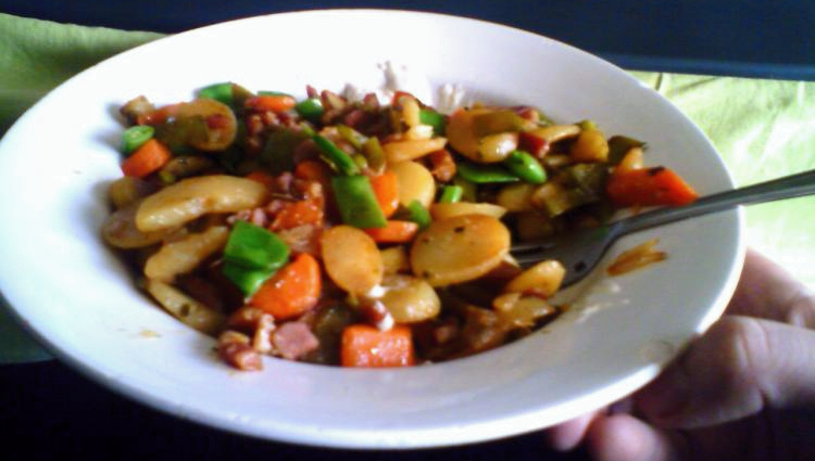 A plate of sliced almond potatoes, mixed vegetables, sliced smoked bacon and garlic.